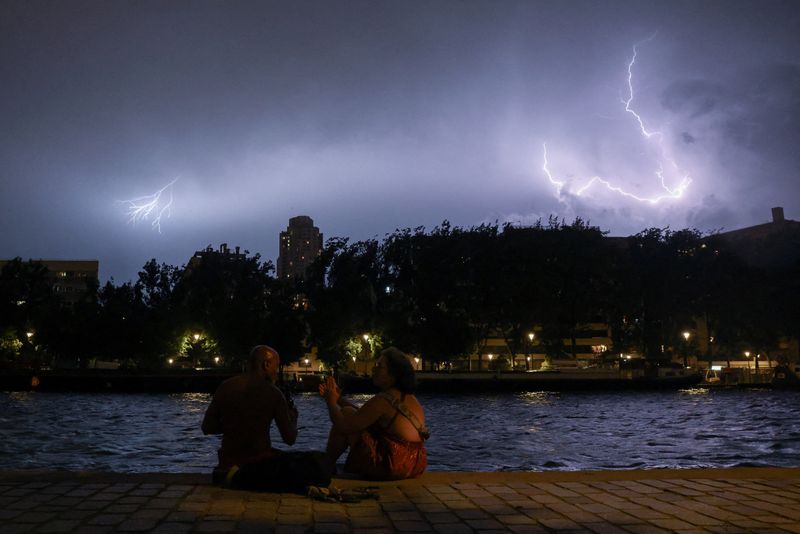 People sit on the banks of the Bassin de la Villette during a storm, as lightning strikes behind them amid a heatwave in Paris, France, June 27, 2026. REUTERS/Tom Nicholson