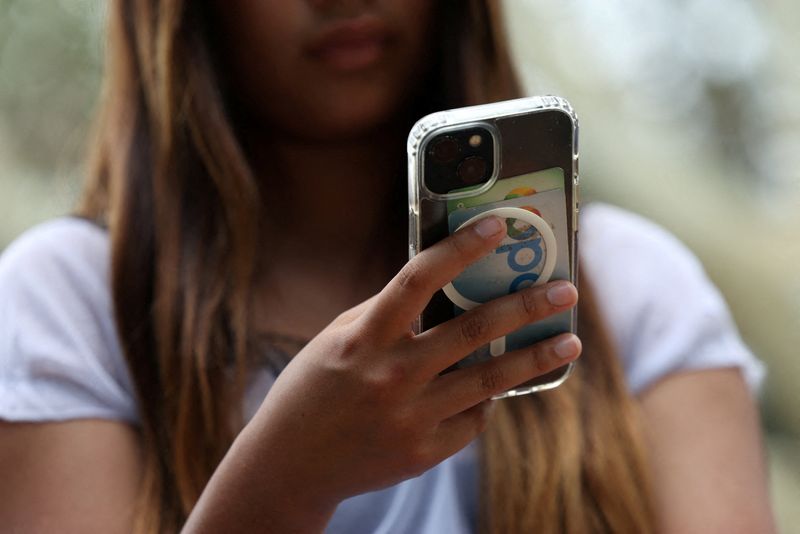 FILE PHOTO: A teenager poses holding a mobile phone as law banning social media for users under 16 in Australia takes effect, in Sydney, Australia, December 10, 2025. REUTERS/Hollie Adams/File Photo