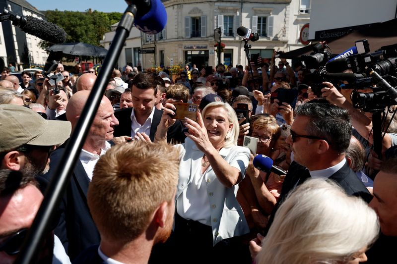 French far-right leader Marine Le Pen makes a selfie with supporters next to Jordan Bardella, president of the French far-right Rassemblement National (National Rally - RN) political party, during a visit at a market in La Fleche, in the Sarthe department, a day after Le Pen announced her candidacy for the 2027 French presidential election following an appeals court ruling that shortened her ban on running for office while upholding her conviction for embezzling EU funds, France, July 8, 2026. REUTERS/Benoit Tessier