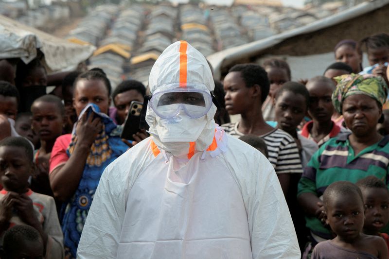 FILE PHOTO: A health worker in personal protective equipment (PPE) stands near displaced people waiting for the burial of suspected Ebola victims at the Kigonze displaced persons camp, one month after an outbreak was declared, in Bunia, eastern Democratic Republic of Congo, June 18, 2026. REUTERS/Gradel Muyisa Mumbere/File Photo