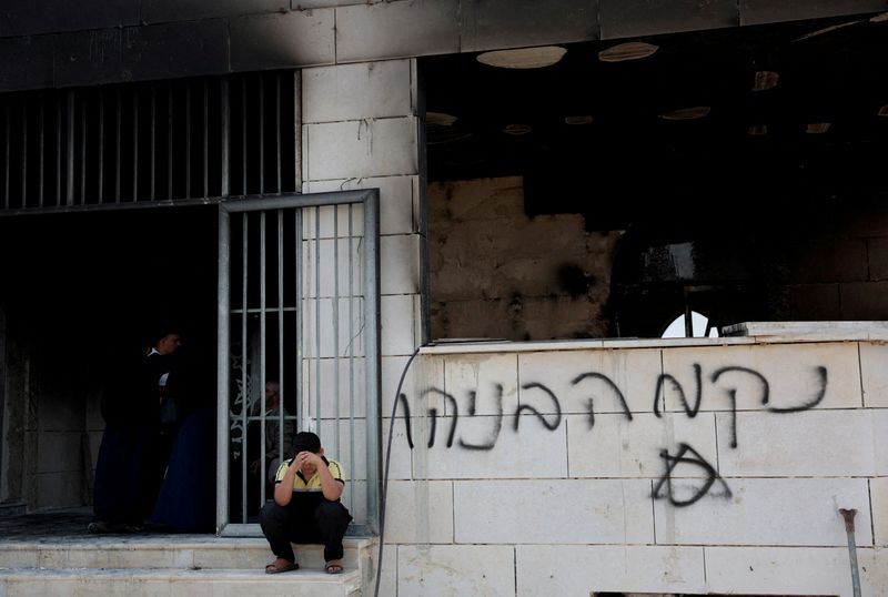 A Palestinian boy sits near a damaged a mosque, which Palestinians say was damaged by Israeli settlers, in Qusra near Nablus, in the Israeli-occupied West Bank, July 26, 2026. Graffiti on the wall reads "Revenge Benayahu", in reference to the 32-year-old Israeli reserve soldier Benayahu Mellet, who was killed in a shooting near the Palestinian village of Tal. REUTERS/Mohamad Torokman
