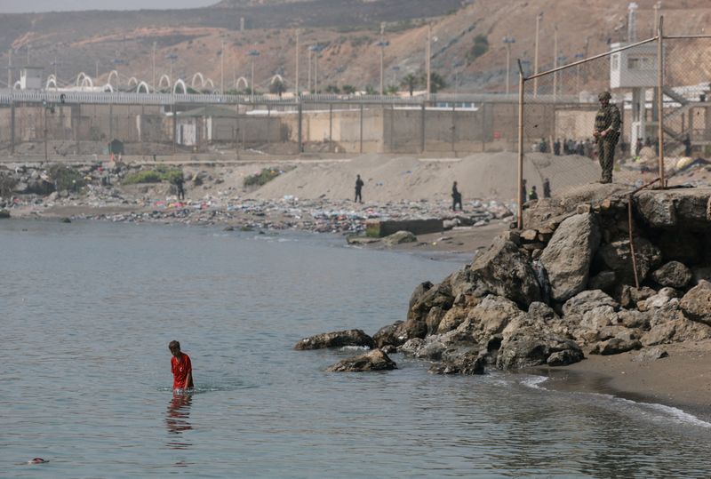 A member of the Spanish security forces stand guard as a migrant minor from Morocco walks in the water after crossing into Ceuta by sea, amid recent mass crossings of migrants on foot and by sea from Morocco into Spanish territory, in Ceuta, Spain, August 1, 2026. REUTERS/Violeta Santos Moura     TPX IMAGES OF THE DAY
