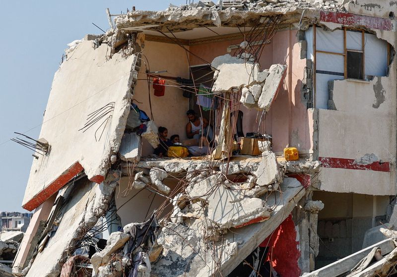 Palestinians sit inside a house damaged during the war, surrounded by destroyed buildings, in Gaza City, August 15, 2026. REUTERS/Mahmoud Issa