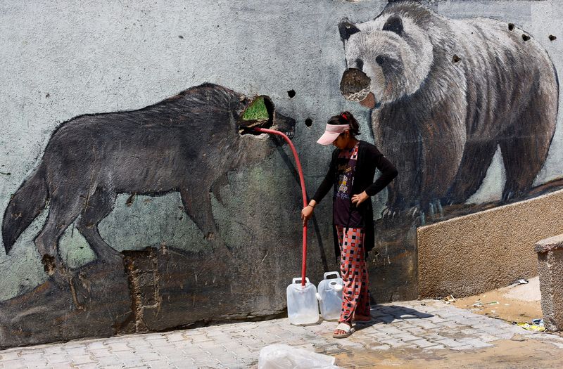 A Palestinian girl fills water containers outside the wall of a zoo damaged during the war, in Gaza City, August 15, 2026. REUTERS/Mahmoud Issa