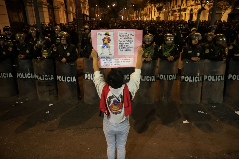 FILE PHOTO: A demonstrator holds a poster as police officers stand guard during a protest against the government of Peru's President Dina Boluarte after Congress approved a partial withdrawal of private pension savings, a measure which could leave millions of Peruvians without retirement funds, in Lima, Peru, September 20, 2025. REUTERS/Sebastian Castaneda/File Photo