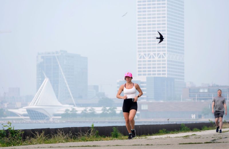 A haze of smoke hovers in the air as Alli Maddelein, of Milwaukee, takes a 5 mile jog through Veteran’s Park in Milwaukee in June 2023.