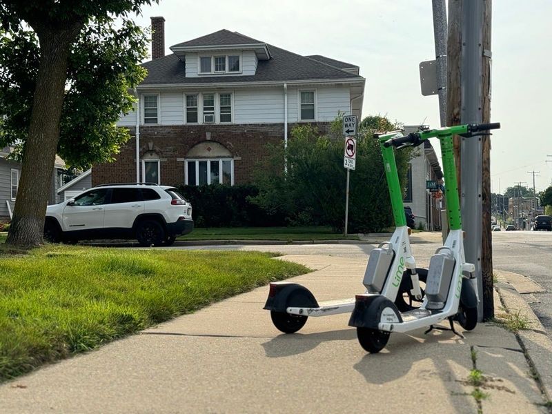 A pair of Lime scooters are shown parked on a Milwaukee sidewalk.