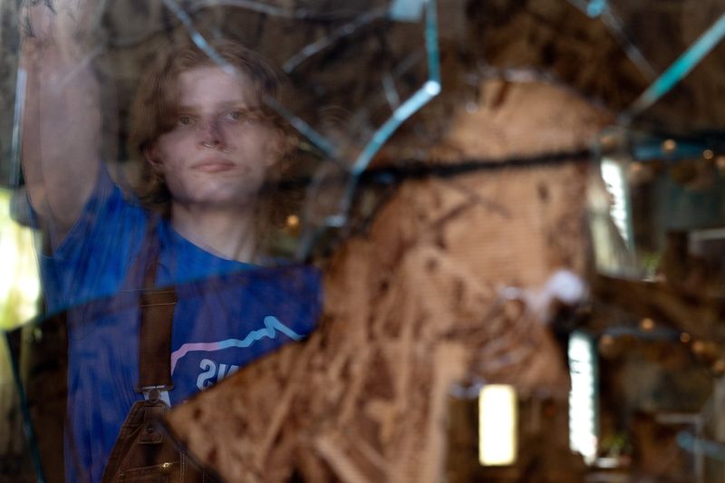 Bartender Porter Pierluissi, 21, peers out the front window of The Sugar Maple, which was recently vandalized, in Milwaukee on July 1, 2025. The Bay View bar’s GoFundMe has already exceeded the funds needed to repair the rock damage from Sunday, June 22.
