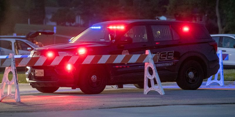 A squad car, its lights flashing, blocks the entrance to the Jaycee Quarry Park as authorities search for a missing swimmer, Tuesday, July 15, 2025, in Sheboygan, Wis.