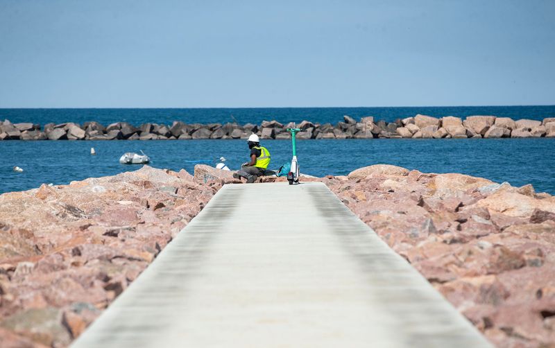 A beach-goer sits at the edge of a pier atop stones meant to stabilize the new South Shore beach, on July 18, 2025.