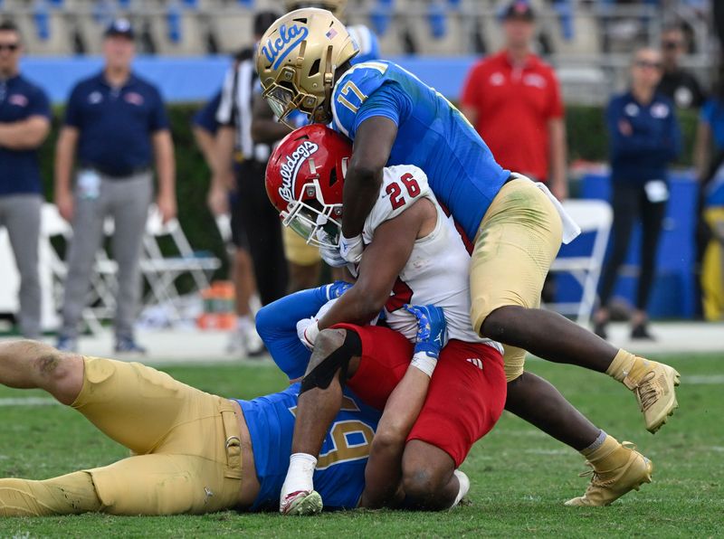 Nov 30, 2024; Pasadena, California, USA; UCLA Bruins linebackers Carson Schwesinger (49) and Jalen Woods (17) tackle Fresno State Bulldogs running back Bryson Donelson (26) during the third quarter at Rose Bowl. Mandatory Credit: Robert Hanashiro-Imagn Images