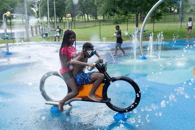 Siblings Shyer Jones, 11, and Ameer Jones, 12, pretend to drive the water motorcycle on the splash pad at Washington Park in Milwaukee on the afternoon of July 23, 2025.