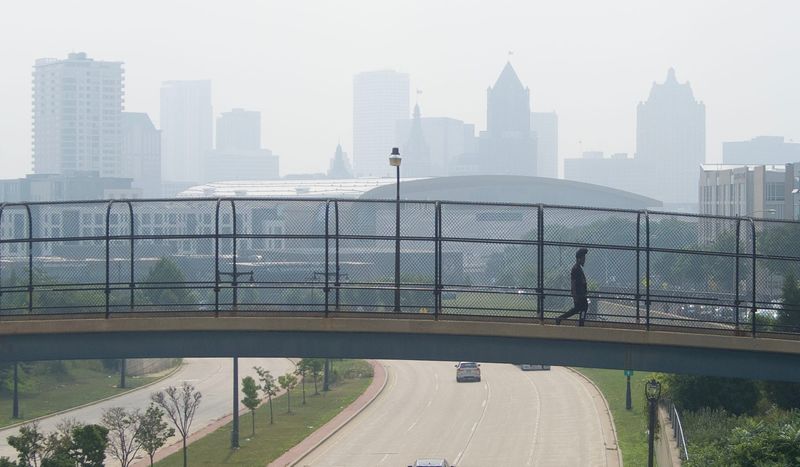 Martrell Lewis, of Milwaukee crosses the pedestrian bridge over West McKinley Avenue to West Winnebago Street as a blanket of smoke fills the air from Canadian wildfires moving south in Milwaukee on July 31, 2025. The Wisconsin Department of Natural Resources issued an air quality advisory for all of the state.