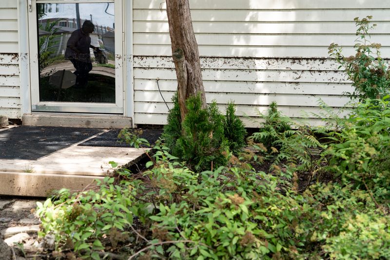Barbara Lewandowska, seen in the door reflection, looks at the flood water line on the outside of her home in Milwaukee on the afternoon of Aug. 11, 2025.