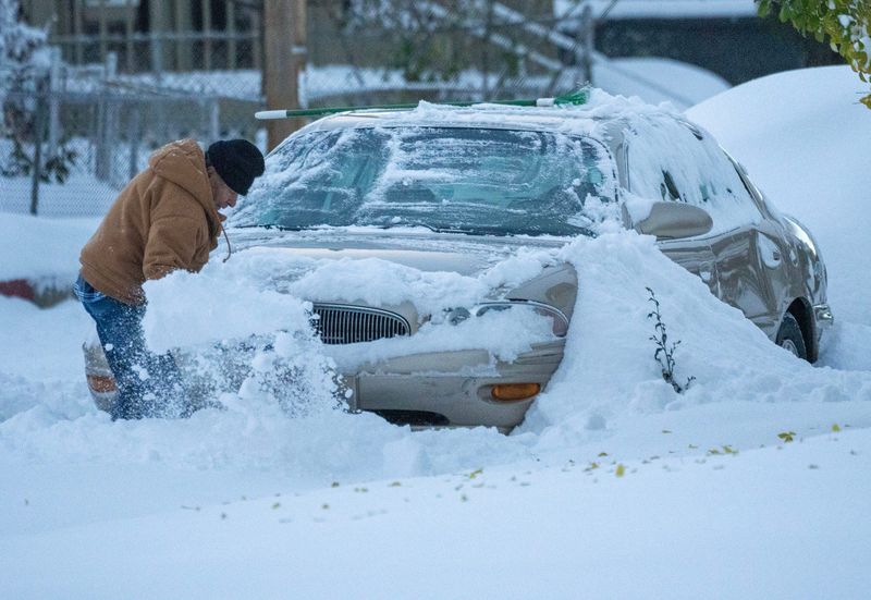 Snow is removed from around a vehicle on Peck Avenue near State Street in Racine, Wisconsin on Nov. 10, 2025. Several inches of lake effect snow fell overnight covering the area.