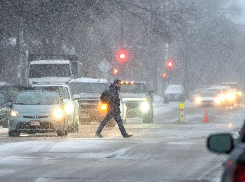 A pedestrian crosses East State Street near North Milwaukee Street past traffic in a the mix of snow and rain in Milwaukee, Wisconsin on Dec. 10, 2025.