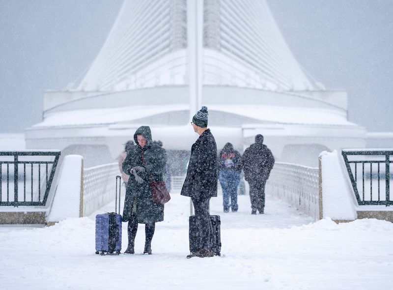 Individuals with suitcase are seen walking past the Milwaukee Art Museum, November 29, 2025, in Milwaukee, Wisconsin. A winter storm was expected to bring 8 to 12 inches of snow to southern Wisconsin.
