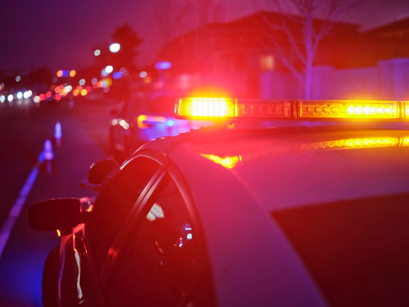 A police car at night alongside a road with emergency lights flashing.