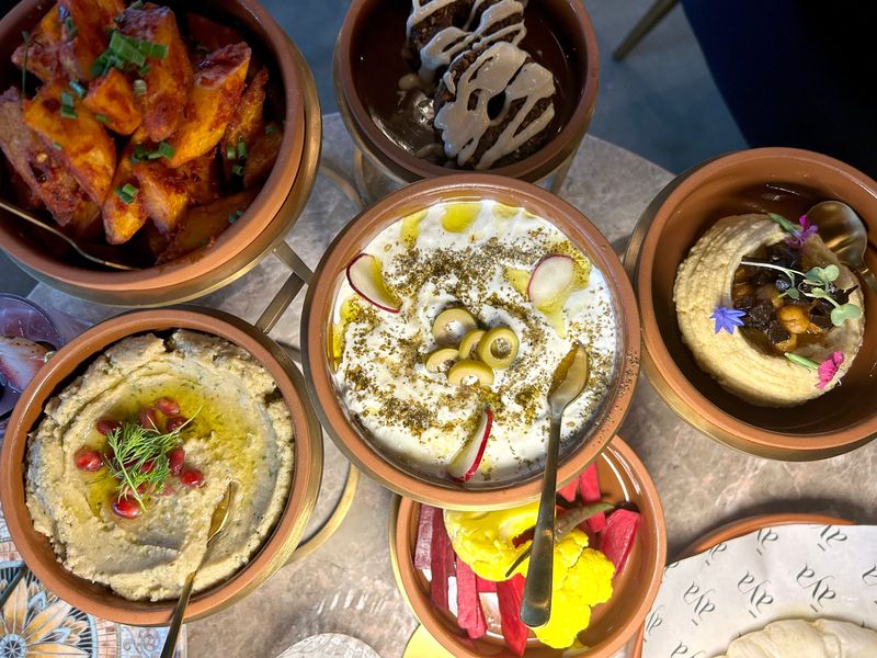 The mezze sampler at āya includes a medley of hummus, batata harra, baba ghanoush, labneh, falafel and pickled vegetables.