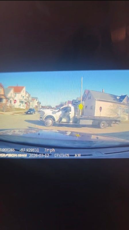 A Milwaukee police officer clings to side of a tow truck in this screenshot taken from a dashcam video recorded by Luis Pizzaro on March 12, 2026. The officer eventually shot the driver, who later died.