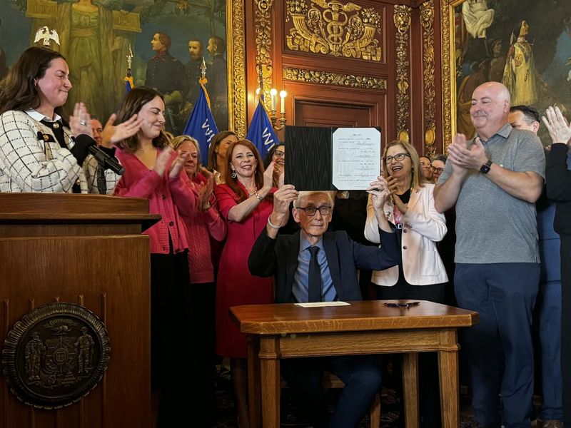 Sophie and Claudia Zeamer, left, and their father, Steve Zeamer, right, celebrate as Gov. Tony Evers signs "Gail's Law" into law. The bill, named for Gail Zeamer, will require insurance companies in Wisconsin to cover secondary breast cancer screenings.