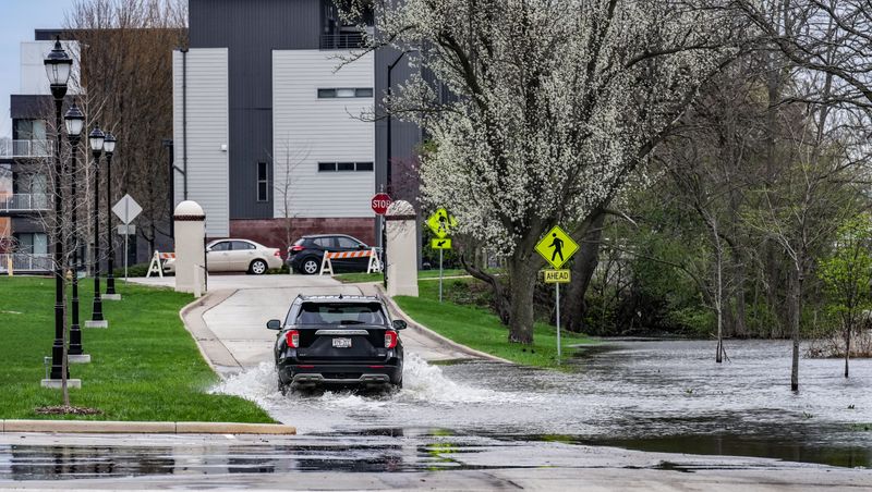 A car drives through flood water on Riverwalk Drive in Waukesha, Wisconsin, on Saturday, April 18, 2026. Multiple days of thunderstorms and heavy rain have caused flooding across southeast Wisconsin.