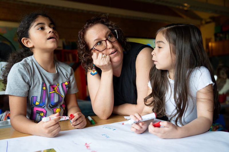 Toni Fink, second-grade teacher at Milwaukee Spanish Immersion School, helps students Elyana and Natalia during a group activity about adjectives on the morning of April 15, 2026, in Milwaukee, Wisconsin.