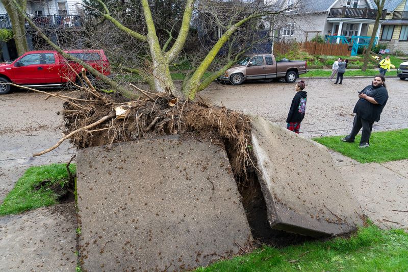 David Machado (far right), 22, and his sister, Yesenia Machado, 17 stand near an uprooted tree that fell on both of David Machado’s trucks near their home along North Booth Street just north of East Locust Street after storms with heavy rain and high winds moved through Milwaukee on April 27, 2026.