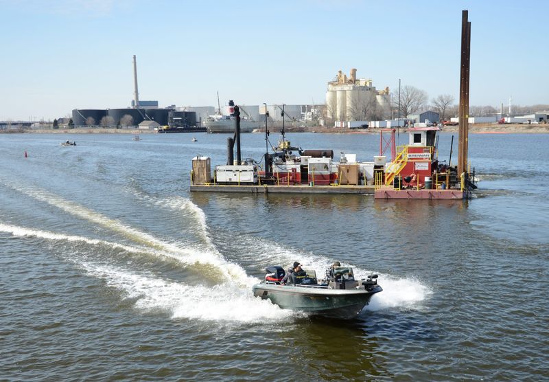 A boater passes a dredging unit as the PCB removal project continues on the Fox River, near the Porlier Street railroad bridge, on April 9, 2014.