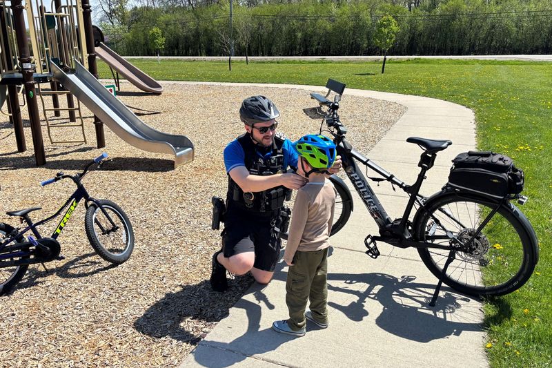 Sgt. Erik Douglas of the Neenah Police Department fits a child with a helmet while on bike patrol.