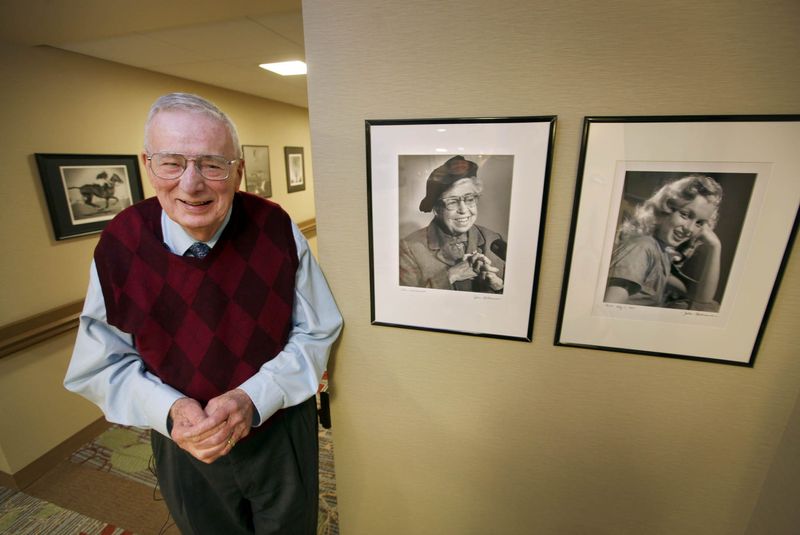 Retired Milwaukee Journal photographer stands next to photographic portraits he made of Eleanor Roosevelt and a young Marilyn Monroe.