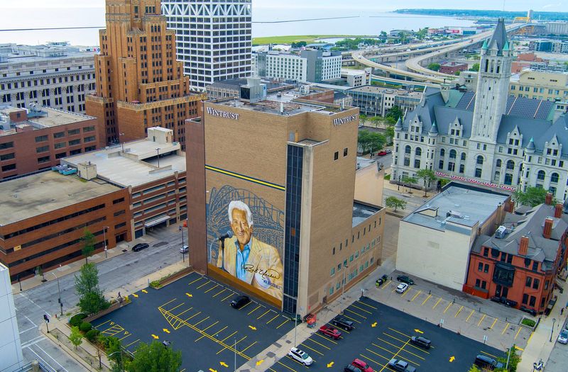 The completed 80-foot by 100-foot mural of Milwaukee Brewers play-by-play announcer Bob Uecker covers the Wintrust Financial Center 731 N. Jackson St. in Milwaukee, Wisconsin on June 26, 2026. A tailgate-themed celebration has been set to mark the completion of “Mr. Baseball,” by Mauricio Ramirez on June 30 featuring brats and the distribution of 500 cans of Miller Lite for a celebratory toast.