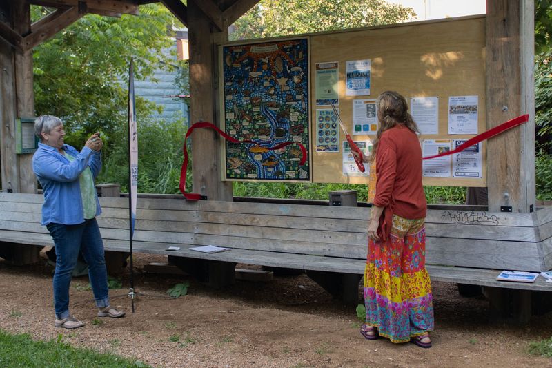 Melanie Ariens, Milwaukee Water Commons, and artist-in-residence Jessica Laub curring the ribbon on one of two mosaics Laub created for the community information board along the Beerline Trail.