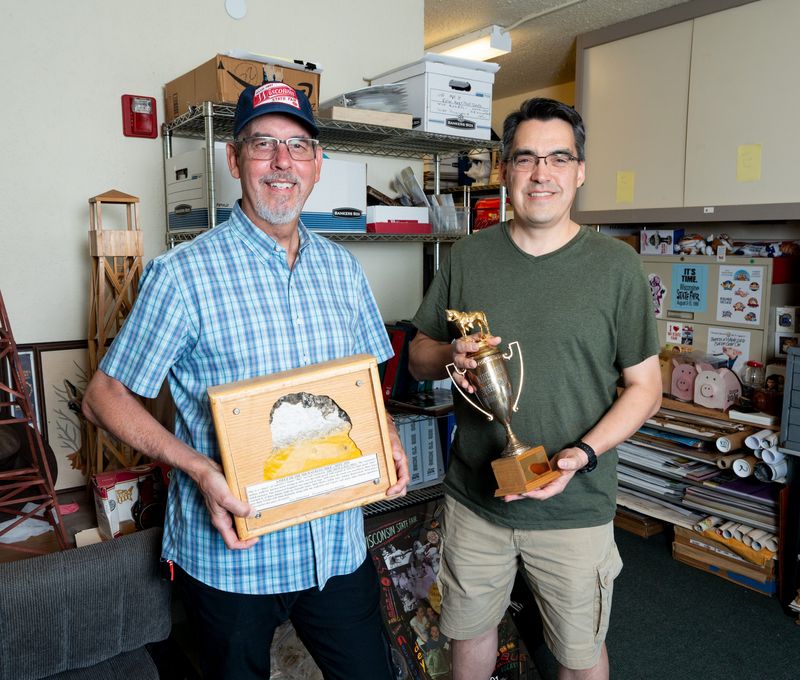 Wisconsin State Fair archivists Tom Zimmerman, left, holding a piece from the Milwaukee Mile from 1955 and Jon Van Beckum, right, holding a Wisconsin State Fair Horse Show trophy from 1957, stand for a portrait in the archive room at the Tommy G. Thompson Youth Center at Wisconsin State Fair Park in West Allis, Wisconsin on July 14, 2026.