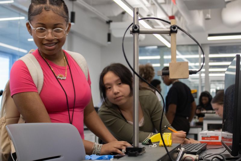At EnQuest, high school rising sophomore Kayla Baker (left) and rising senior Nansy Vue watch a tensile testing machine operate while recording data from their mice bones and polymers at UMW's Engineering and Mathematics Building on July 29, 2026.
